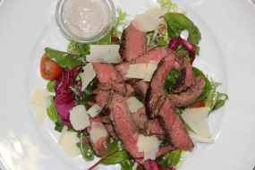 200g Grilovaný hovězí steak krájený na plátky, listy rukoly, cherry tomaty, olivový olej,  hobliny sýru Grana Padano